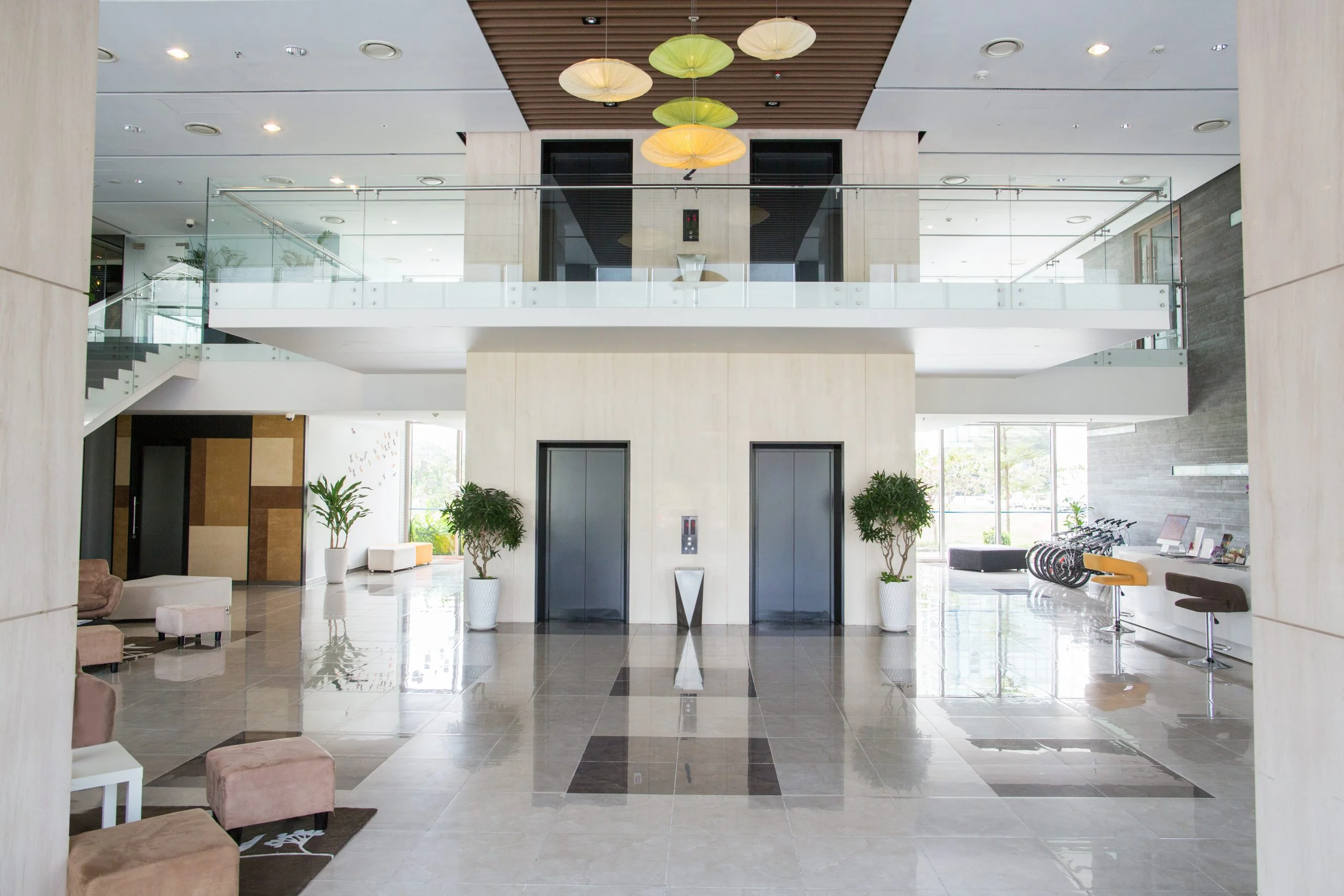 Modern lobby with floor-to-ceiling glass walls, glass railings on the second floor, and glass doors on the elevators.